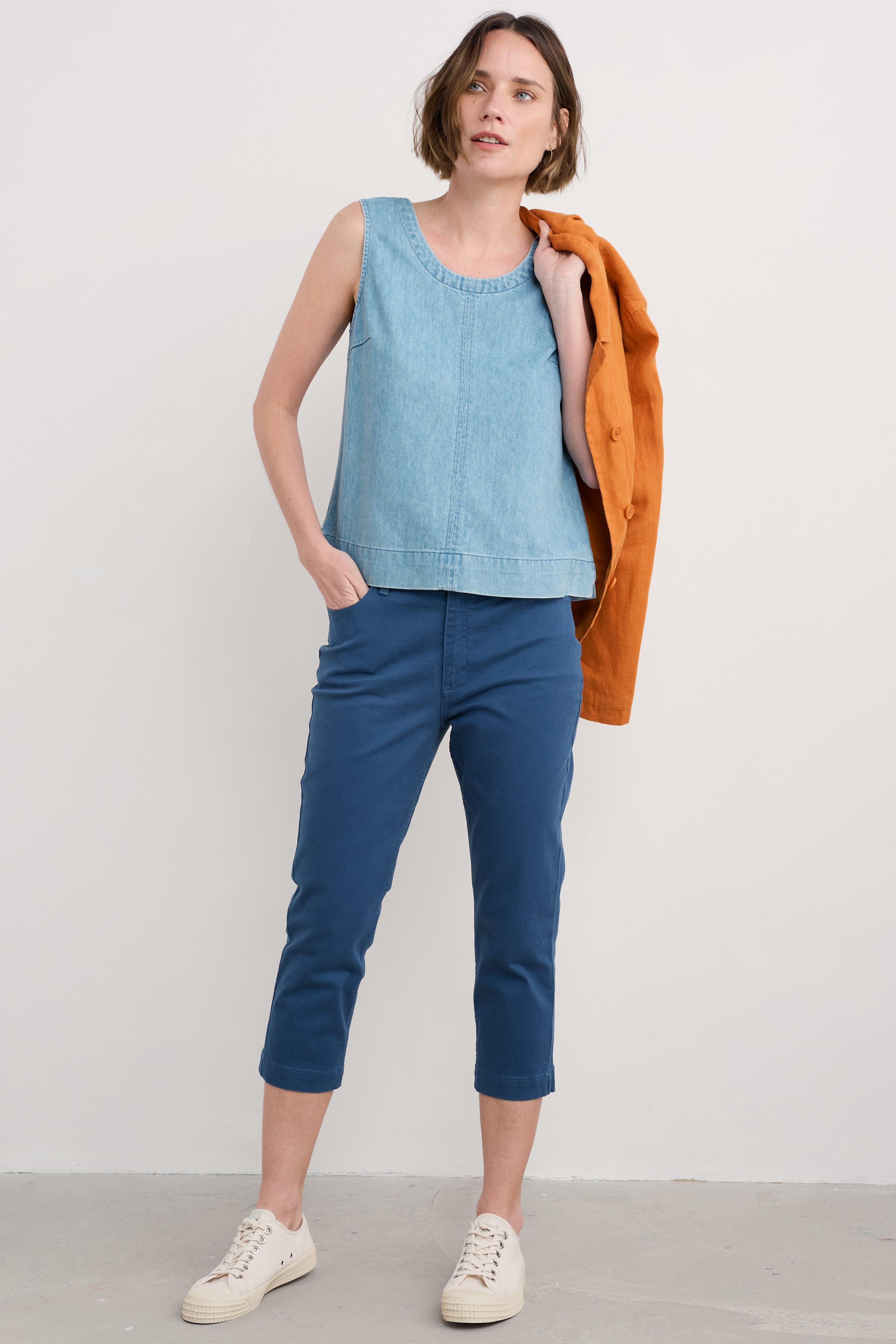Model wearing blue organic cotton slim fit cropped trousers, paired with blue sleeveless top and white sneakers.