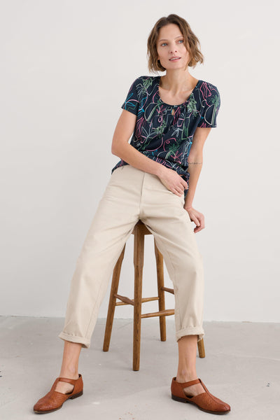Full seated view of the woman in the T-shirt and trousers, leaning back on her arms.
