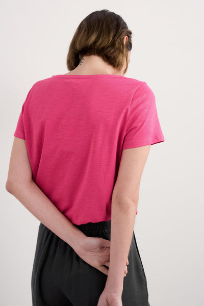 Back view of model wearing organic cotton pink t-shirt with arms crossed behind back.