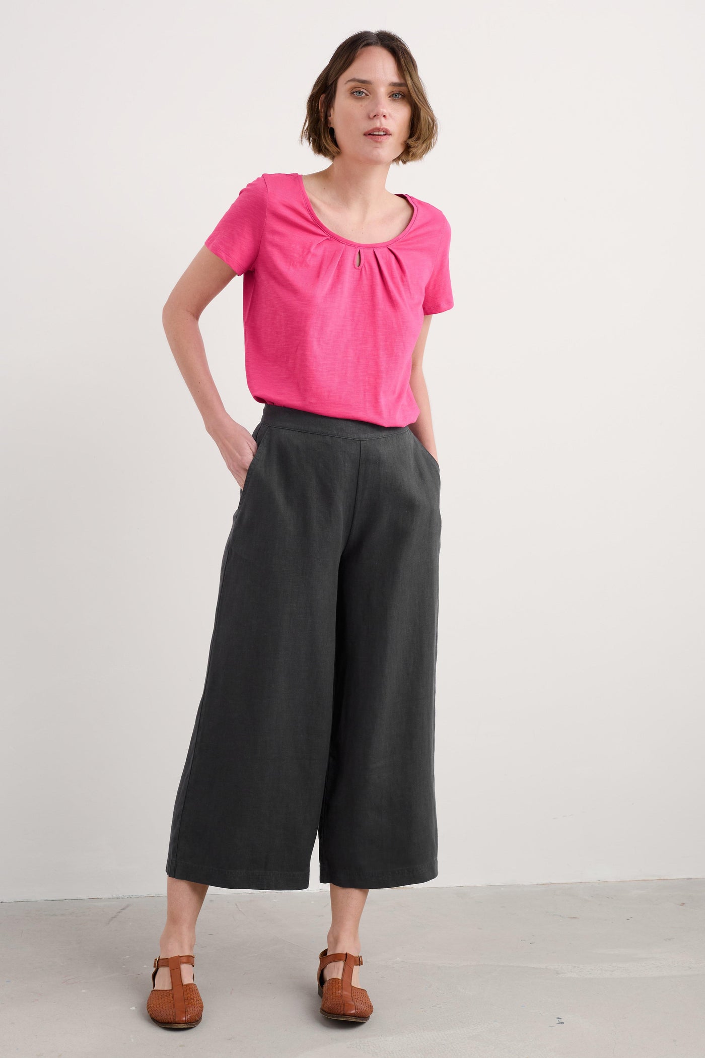 Woman wearing a pink Seasalt Appletree T-shirt with scoop neck paired with black trousers and brown shoes.