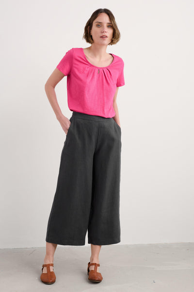 Woman wearing a pink Seasalt Appletree T-shirt with scoop neck paired with black trousers and brown shoes.