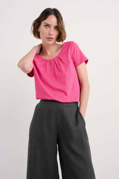 Woman standing wearing pink organic cotton t-shirt paired with black wide trousers.