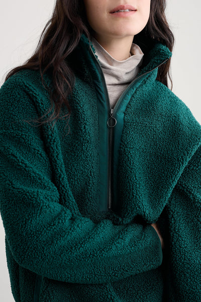 Person wearing a green fleece jacket with half zip on a plain background