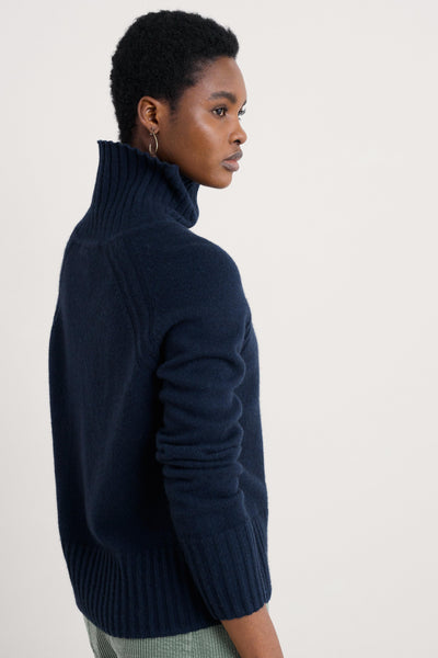 Person wearing a knitted wool jumper with a ribbed roll neck on a light background