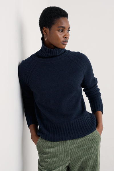 Person wearing a navy merino wool sweater and green pants against a white background