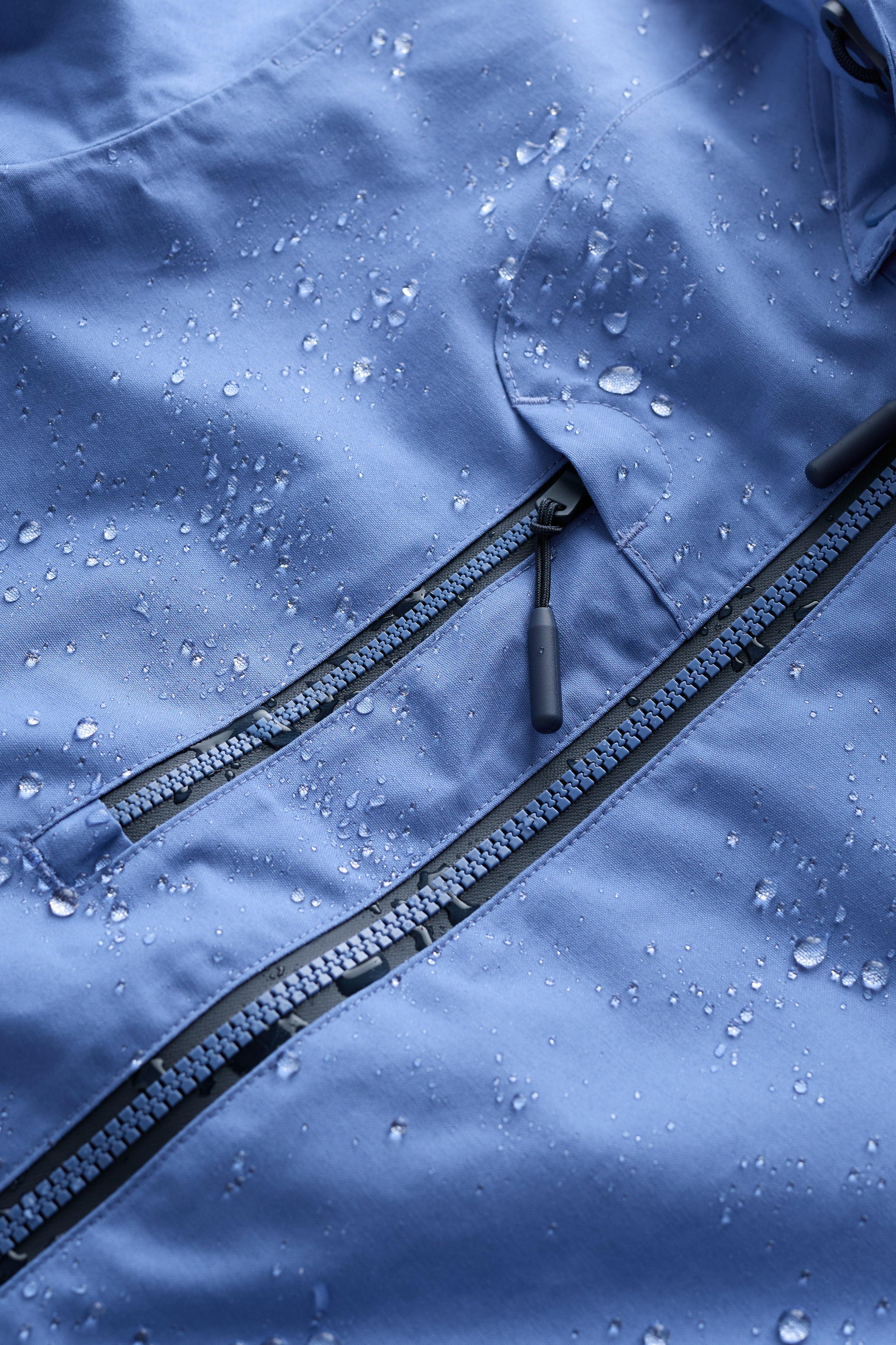 Close-up of a blue jacket with water droplets on the fabric and zipper.