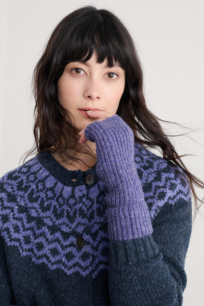Woman wearing a dark sweater with a patterned collar and purple merino wool mittens against a plain background