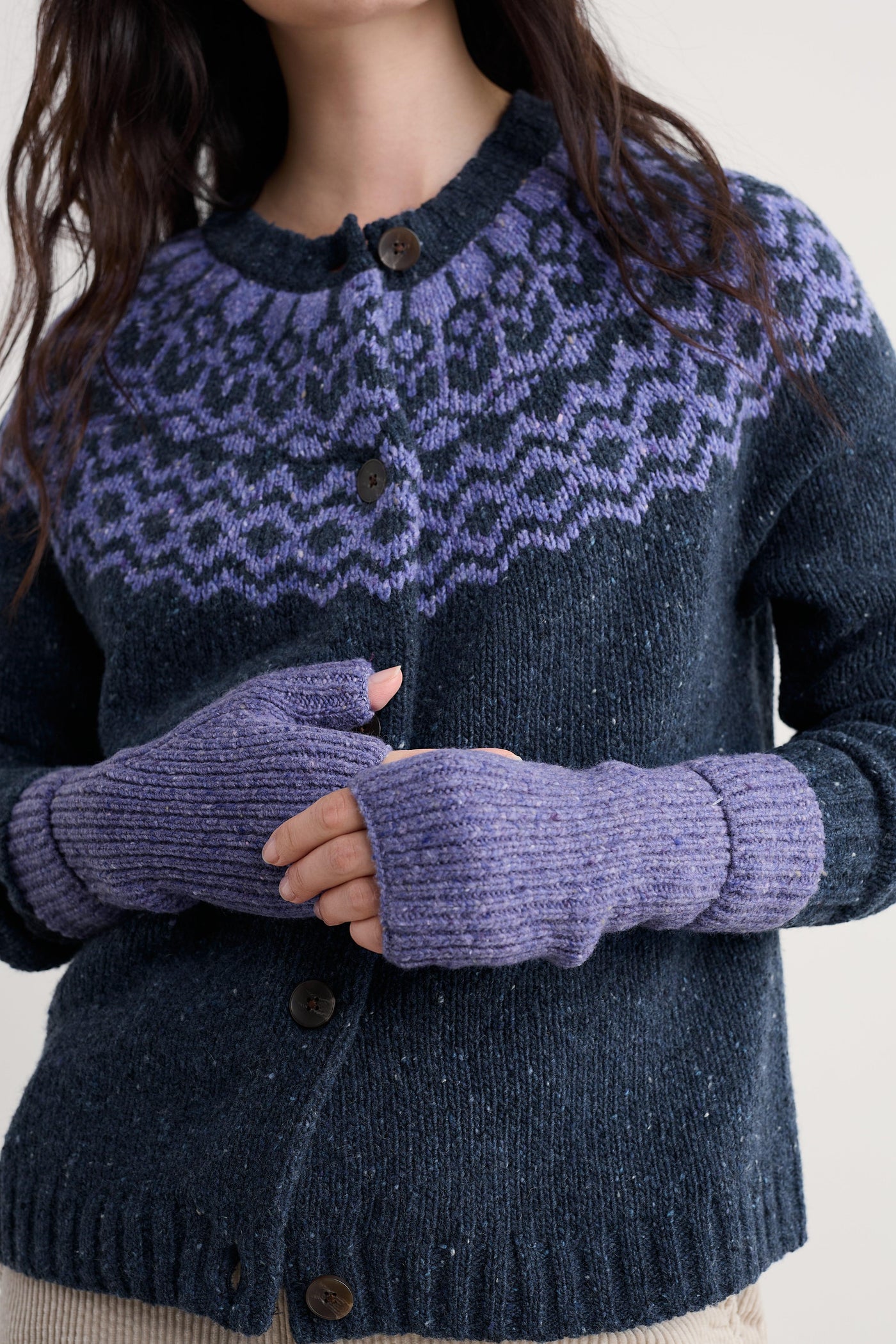 Person wearing a dark blue knitted cardigan with purple patterned yoke and matching fingerless gloves.