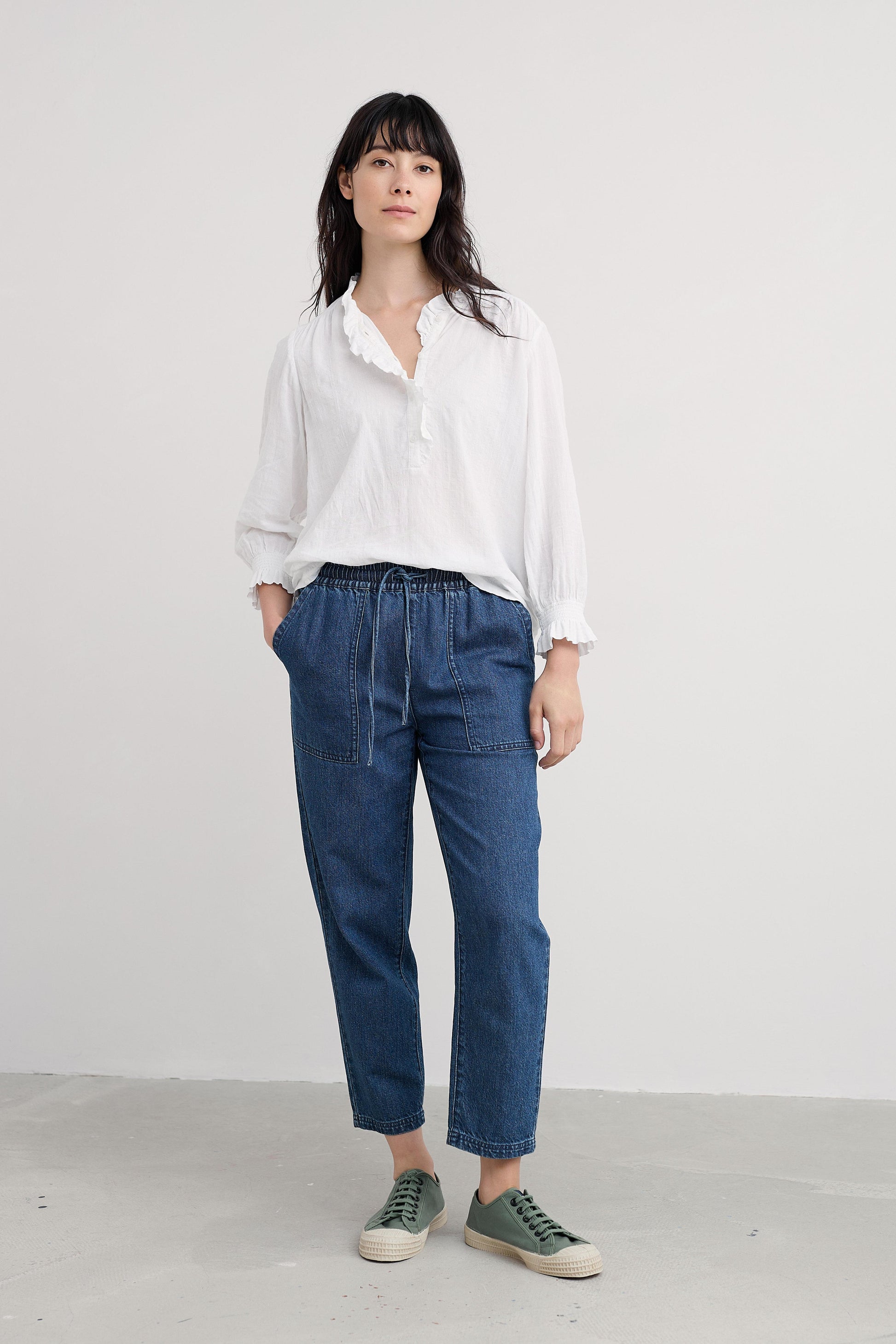 Woman wearing a white organic cotton shirt and blue pants against a plain background