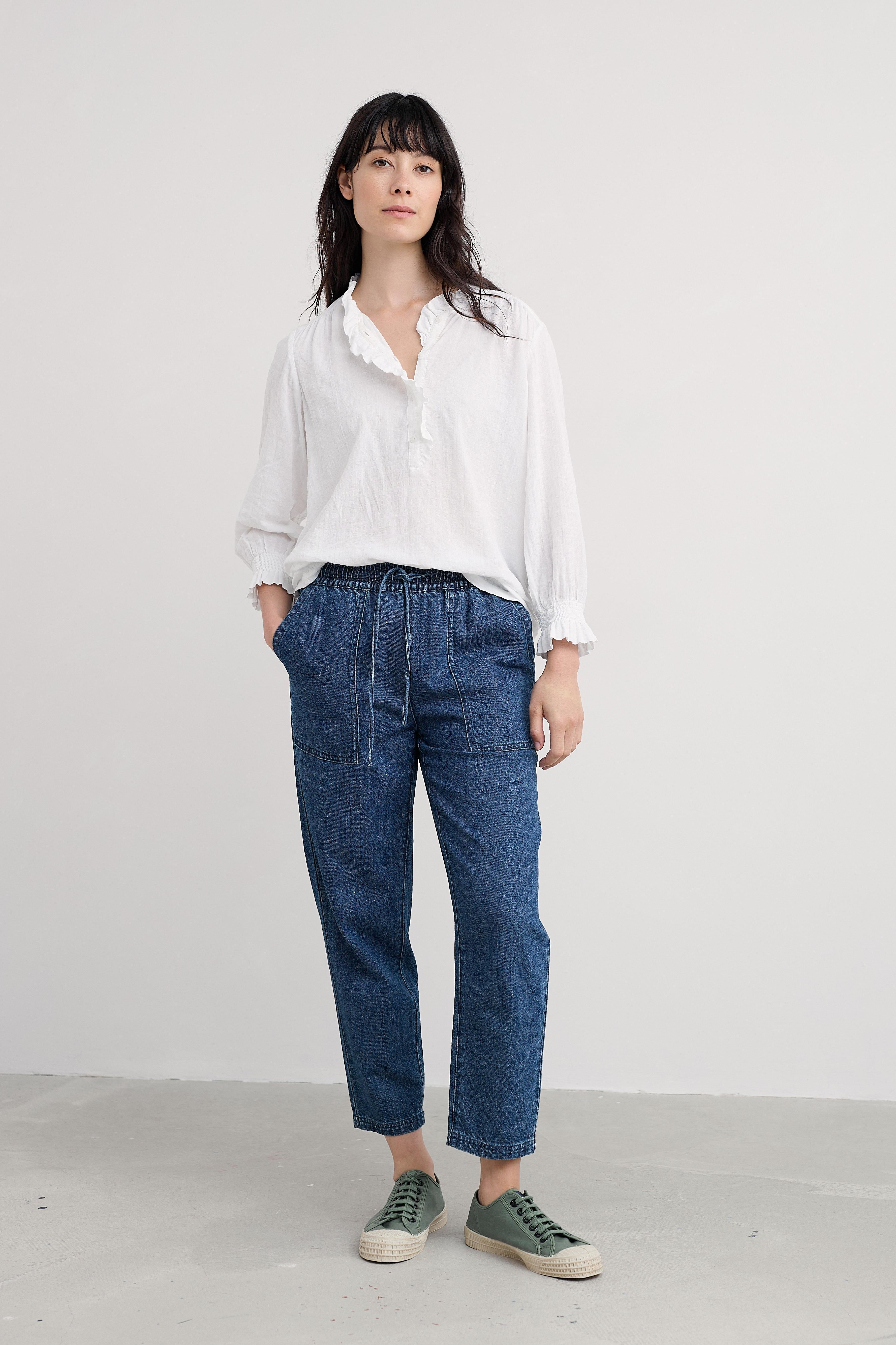 Woman wearing a white organic cotton shirt and blue pants against a plain background