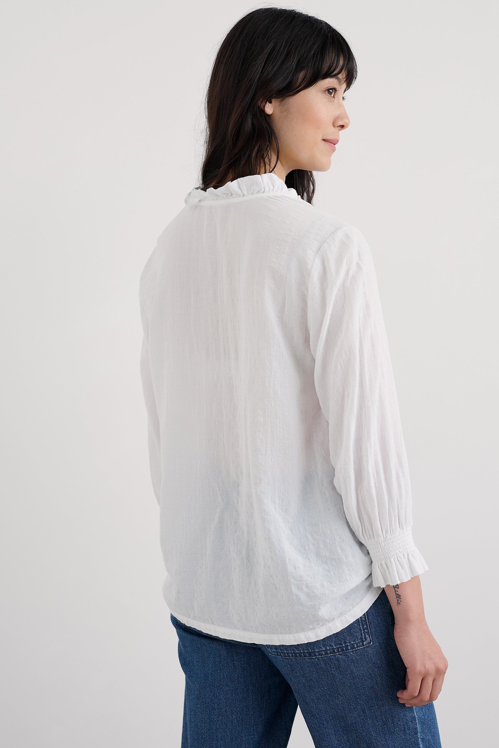 Woman wearing a white blouse and blue jeans on a plain background