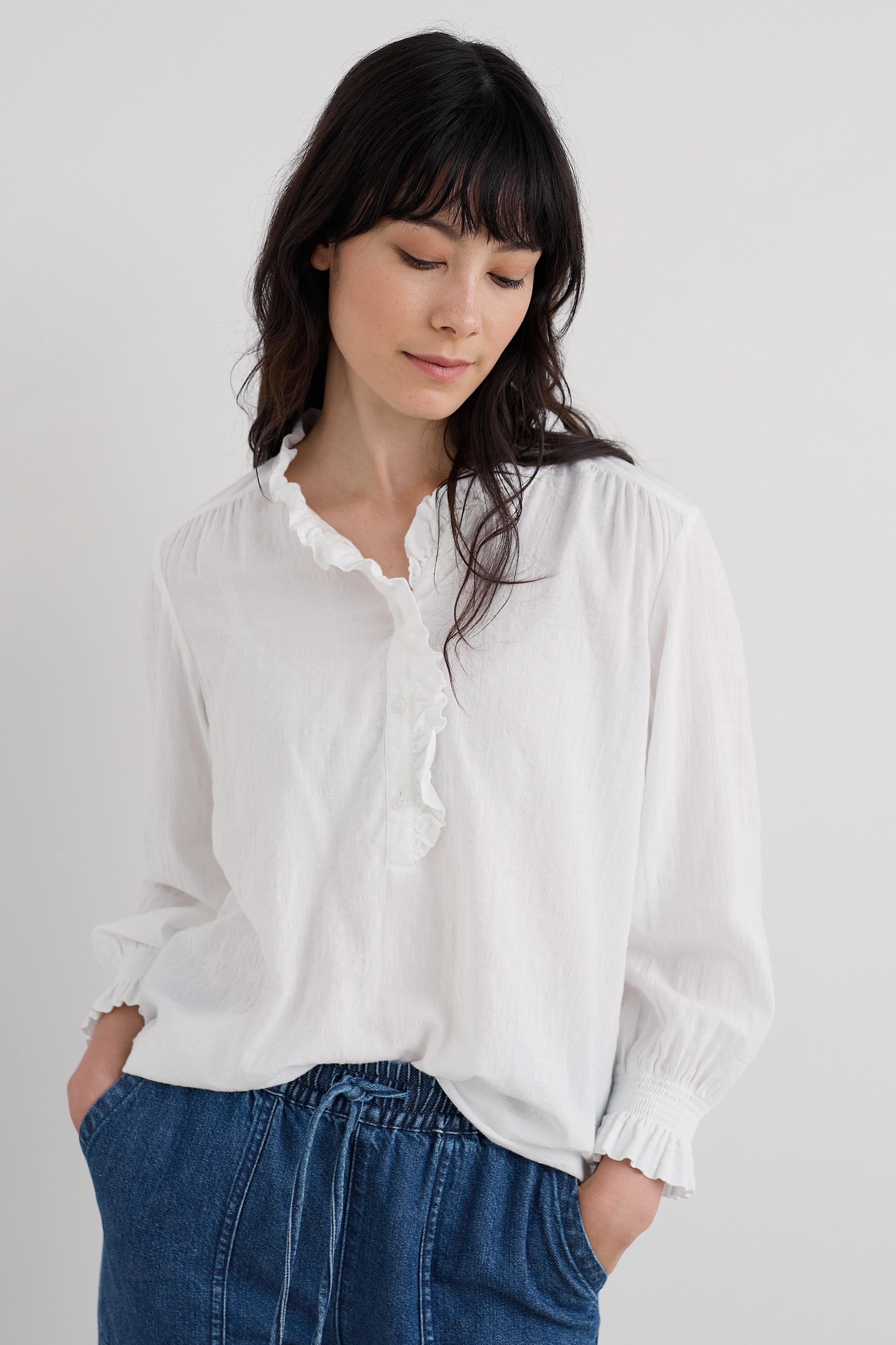 Woman wearing a white organic cotton blouse and blue jeans against a plain background