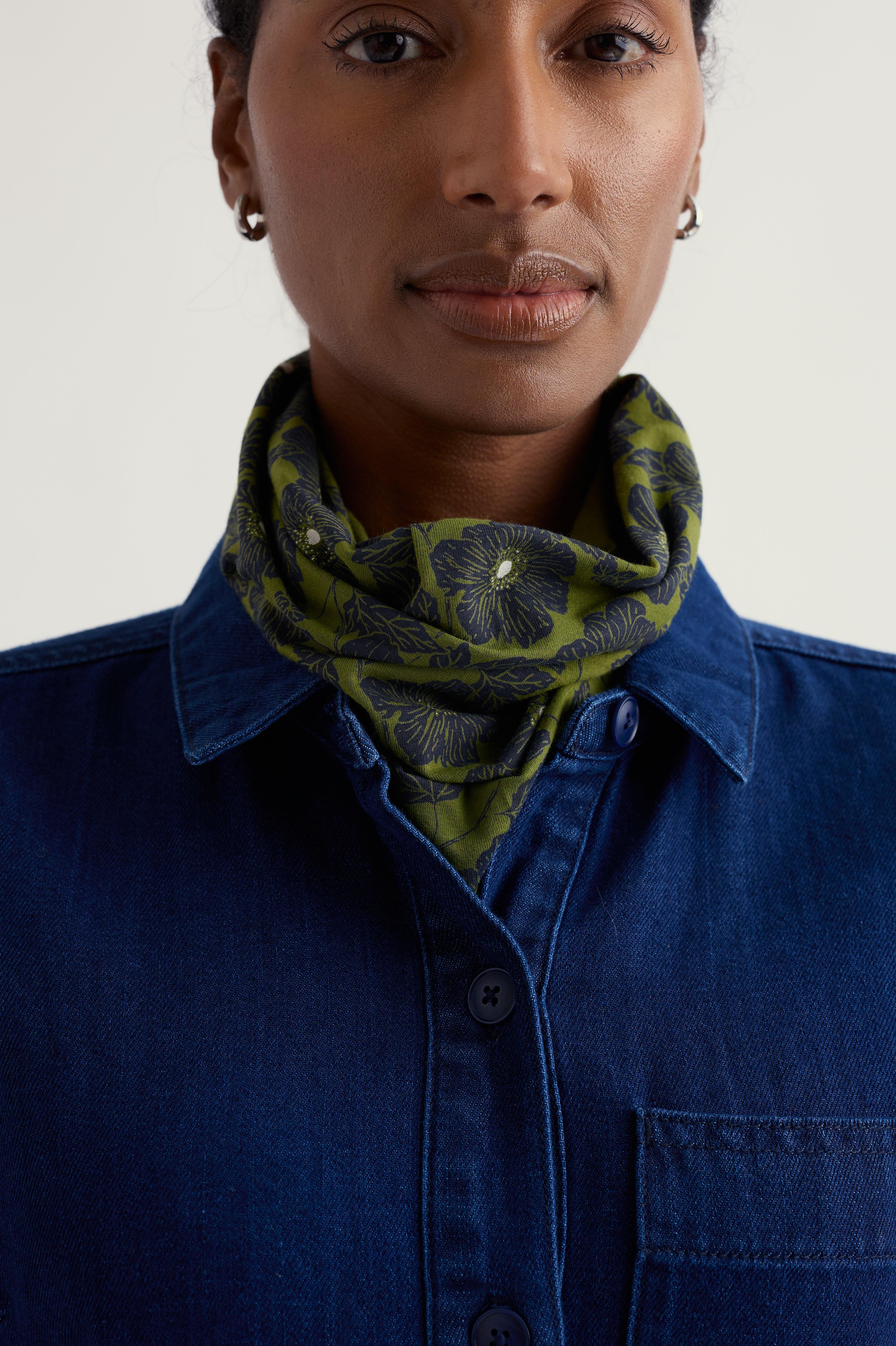 Woman wearing a blue shirt and green patterned scarf against a plain background