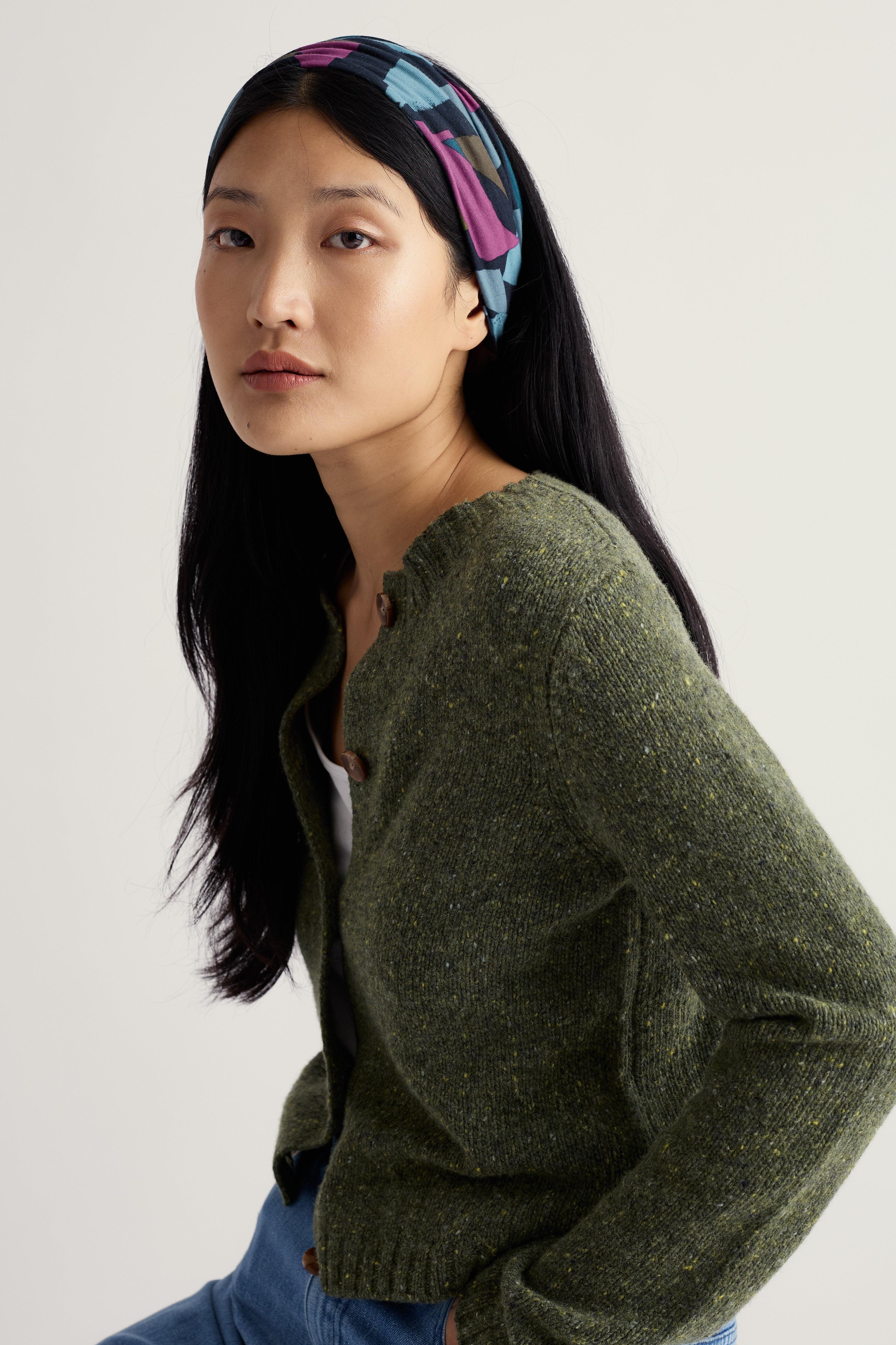 Woman wearing a green sweater and colorful organic cotton headband against a plain background