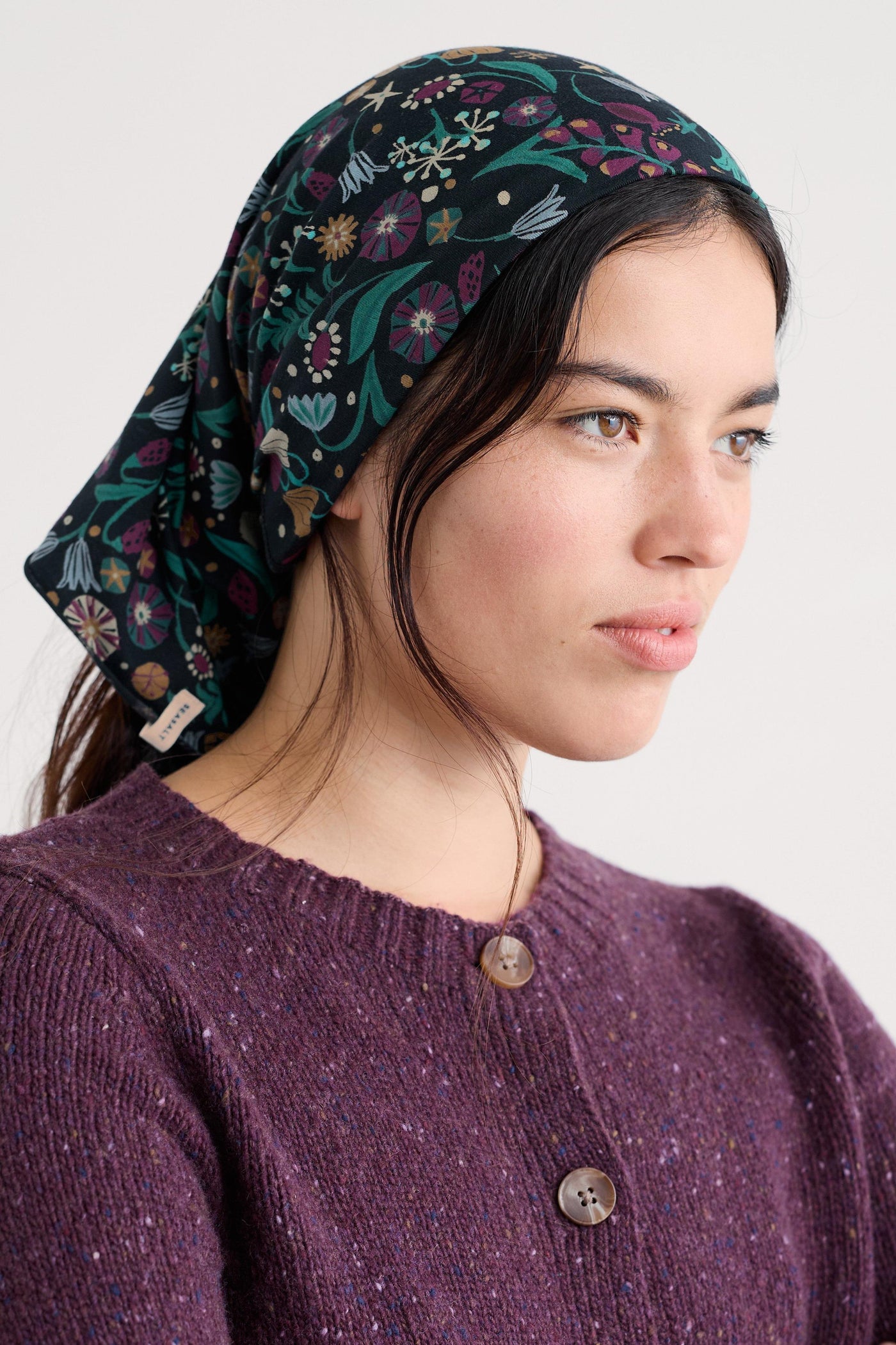 Woman wearing a patterned headscarf and a purple wool sweater on a white background