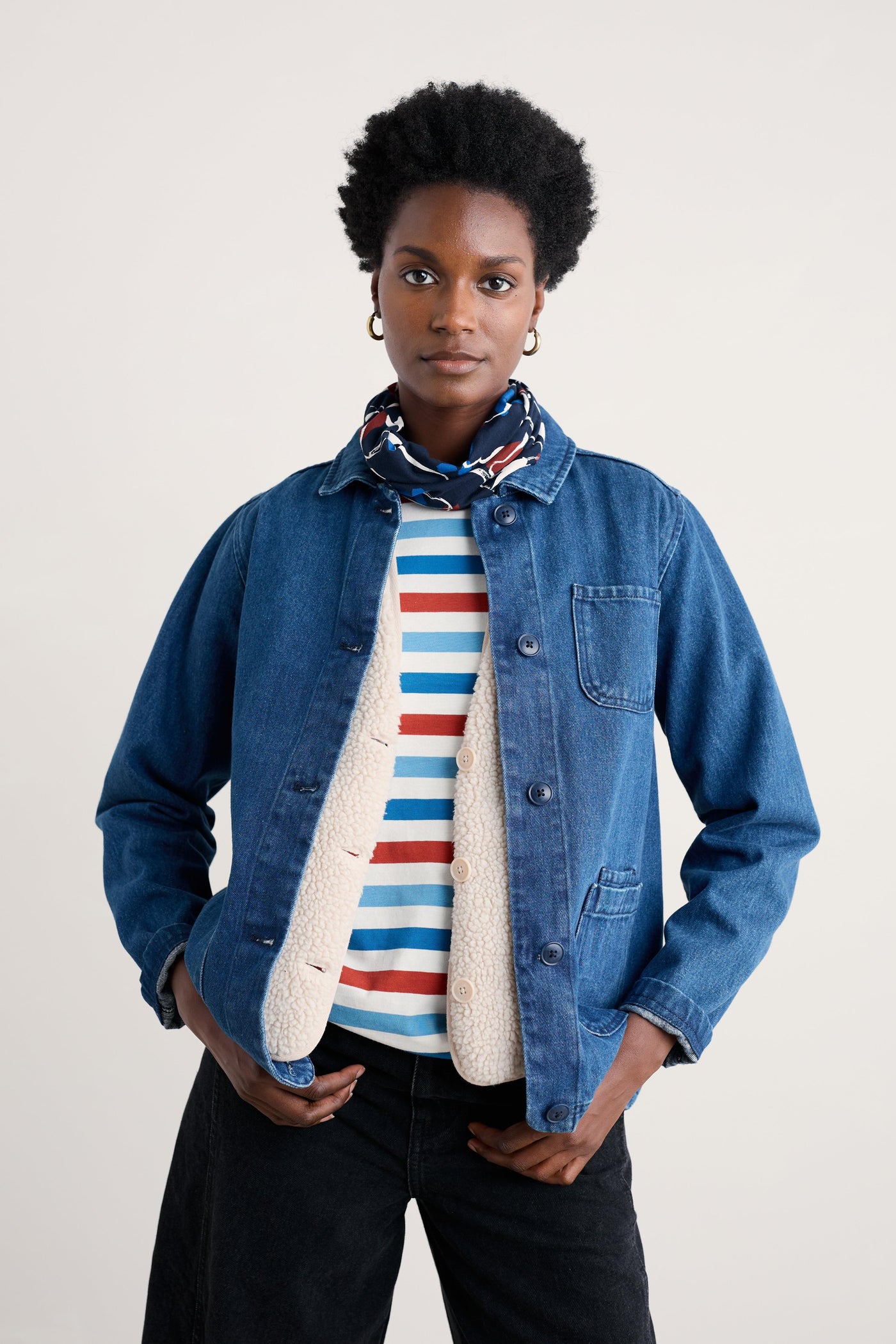 Person wearing a denim jacket over a striped sweater with a plain background