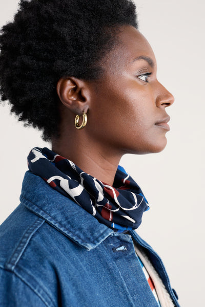 Woman wearing a blue denim jacket with a patterned organic cotton scarf around her neck against a plain background