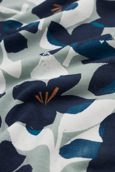 Close-up of floral organic cotton fabric with blue, white, and orange flowers on a light gray background