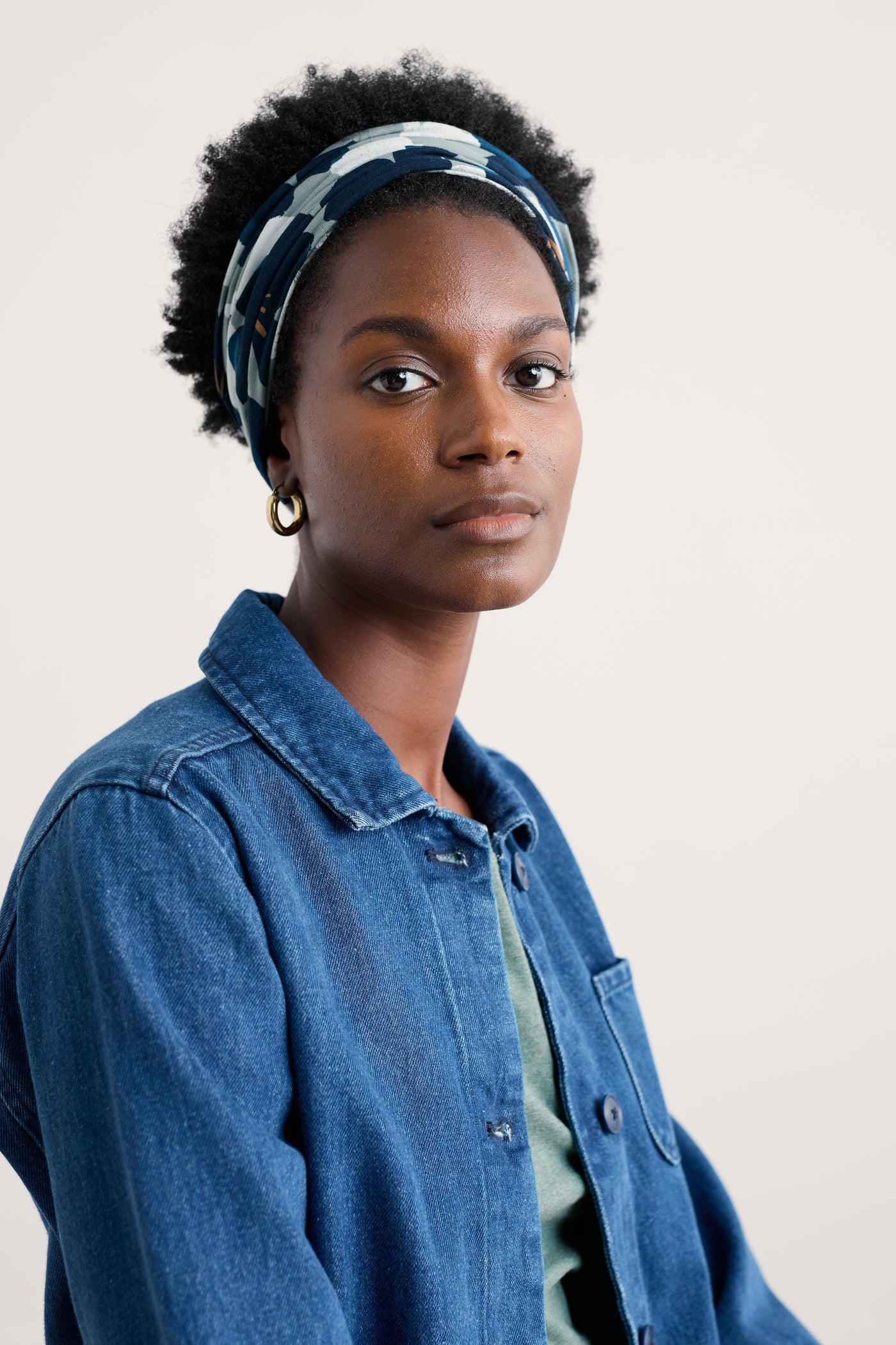 Woman wearing a blue denim jacket and patterned organic cotton headband against a plain background