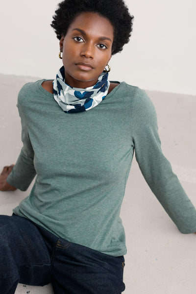 Woman wearing a green long-sleeve shirt and a patterned organic cotton scarf on a light background