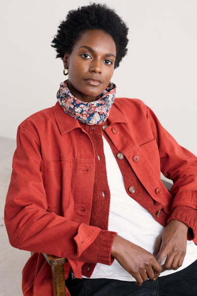 Person wearing a red jacket over a floral scarf and white shirt on a plain background