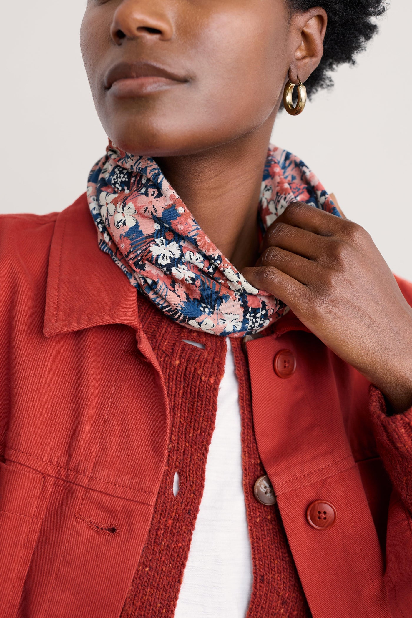 Woman wearing a red jacket with a floral organic cotton scarf around her neck against a white background