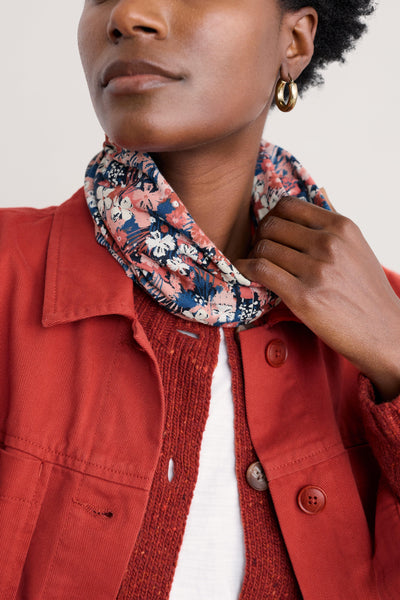 Woman wearing a red jacket with a floral organic cotton scarf around her neck against a white background