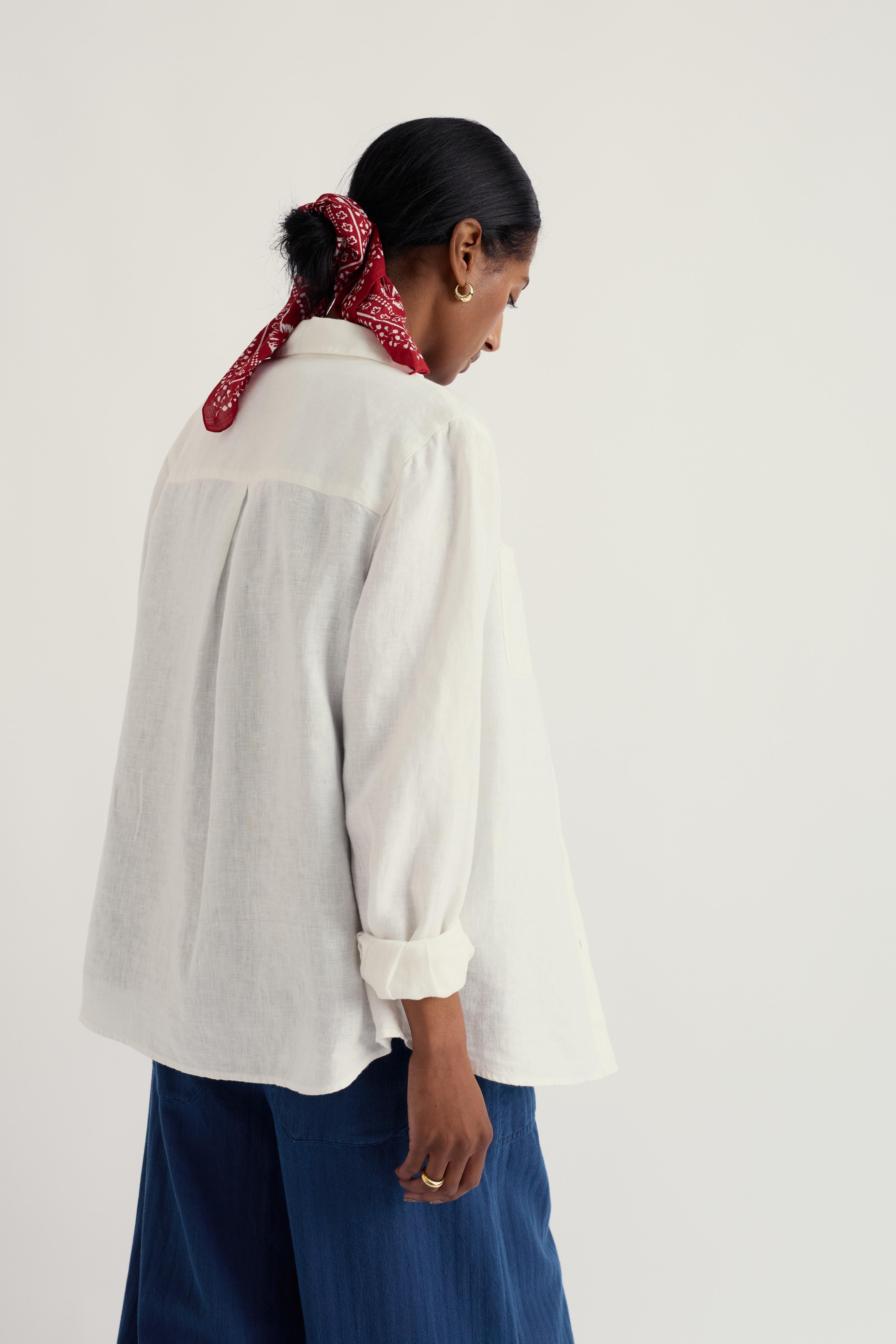 Person wearing a white linen shirt and blue pants with a red patterned headscarf on a light gray background