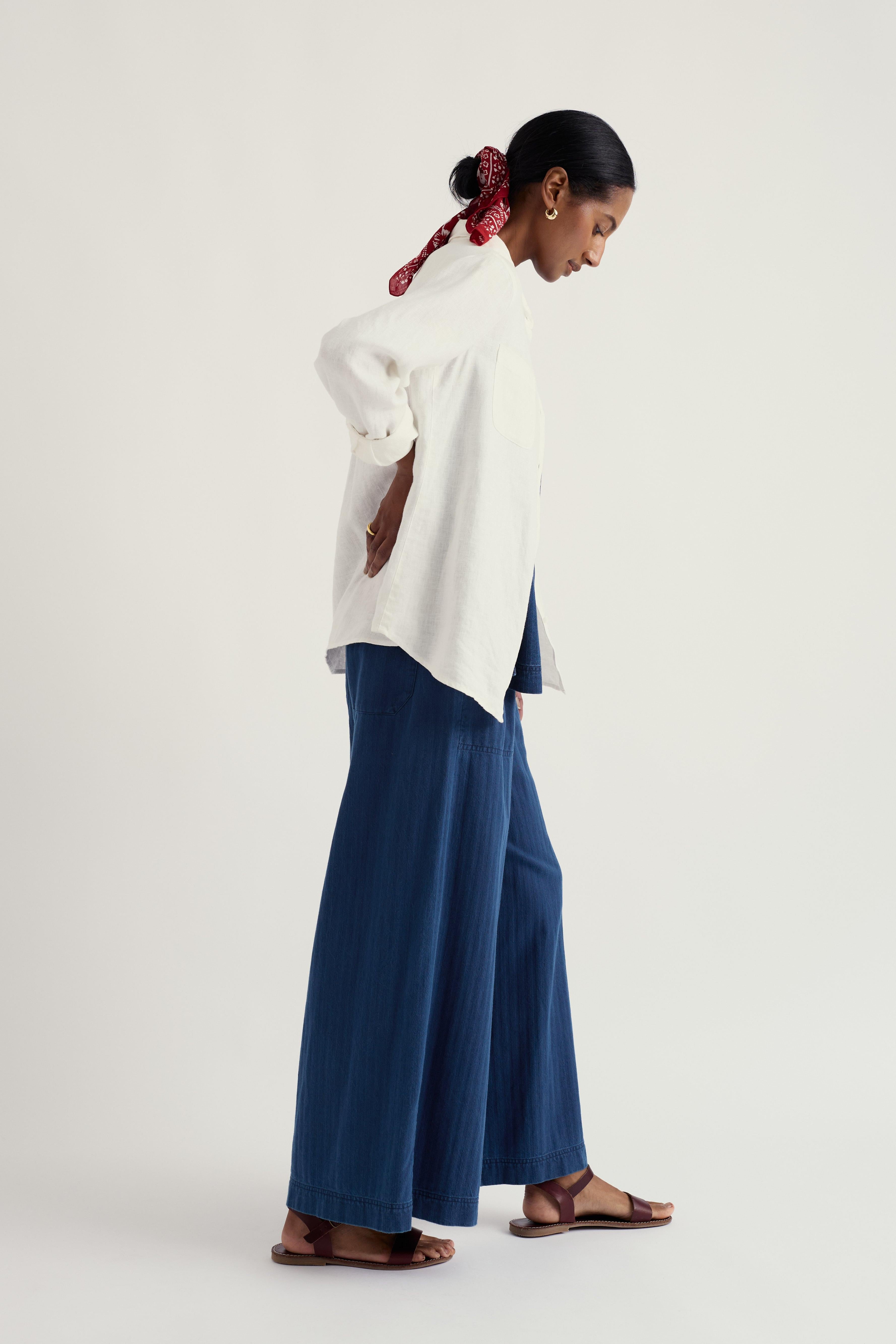 Woman wearing a white linen shirt and blue pants on a light gray background