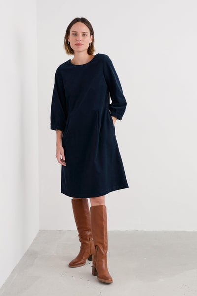 Woman wearing a navy dress and brown knee-high boots on a white background