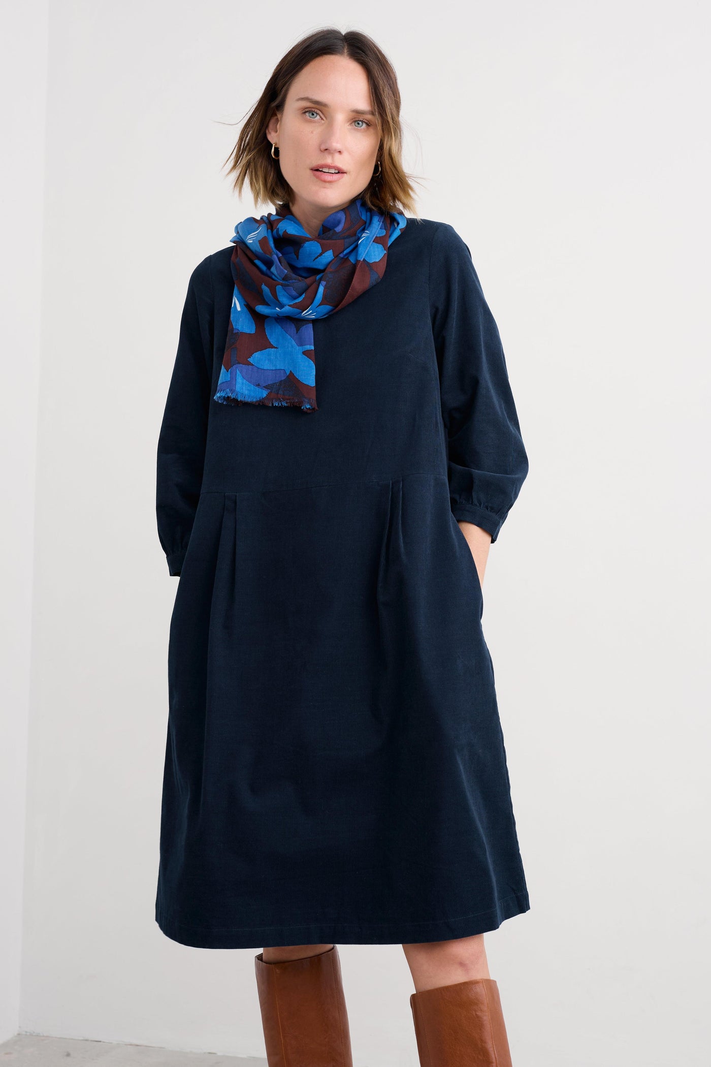 Woman wearing a navy organic cotton dress with a blue patterned scarf against a white background