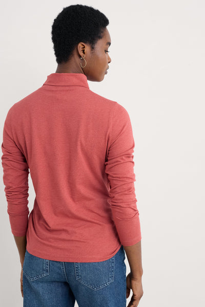 Person wearing a pink long-sleeve shirt and blue jeans on a light gray background