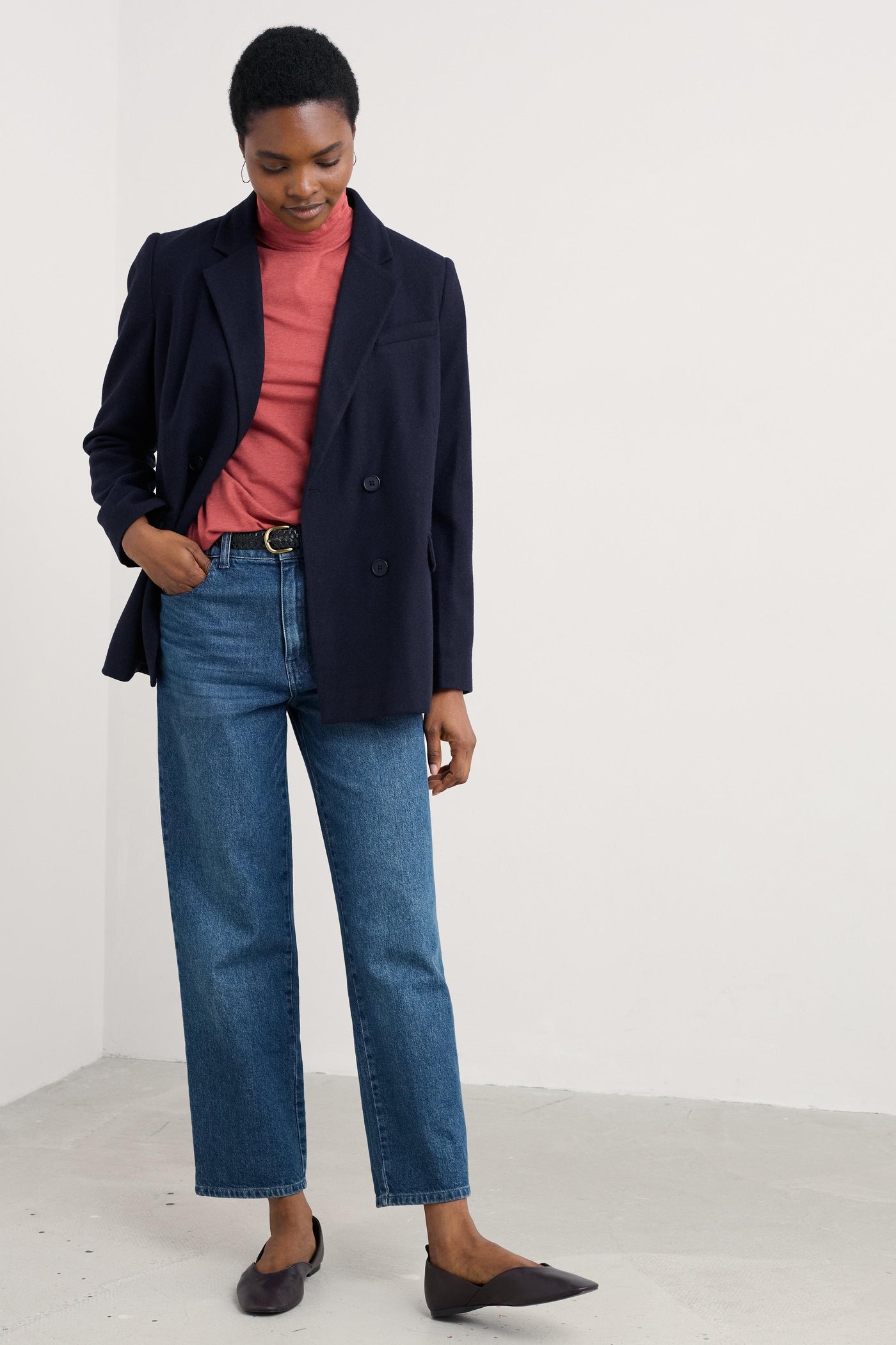 Person wearing a navy blazer, organic cotton pink shirt, and blue jeans on a white background