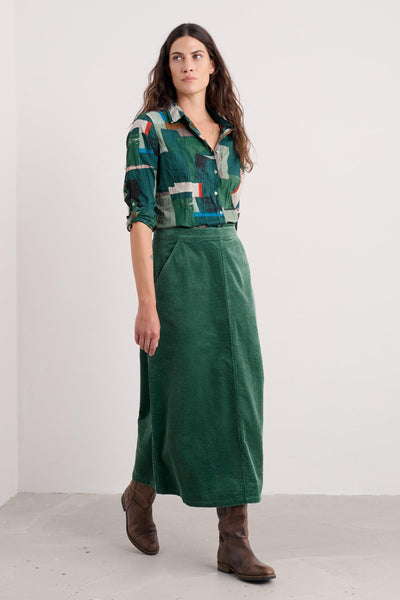 Woman wearing a patterned organic cotton shirt and green skirt against a white background