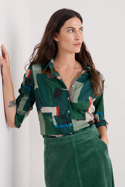 Woman wearing a green abstract patterned shirt and green cord skirt against a white background