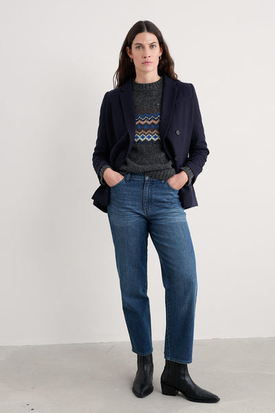 Woman wearing a dark wool blazer, patterned sweater, blue jeans, and black boots on a white background