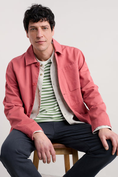 Model sitting on stool wearing green and white striped long sleeve top paired with coral shacket.