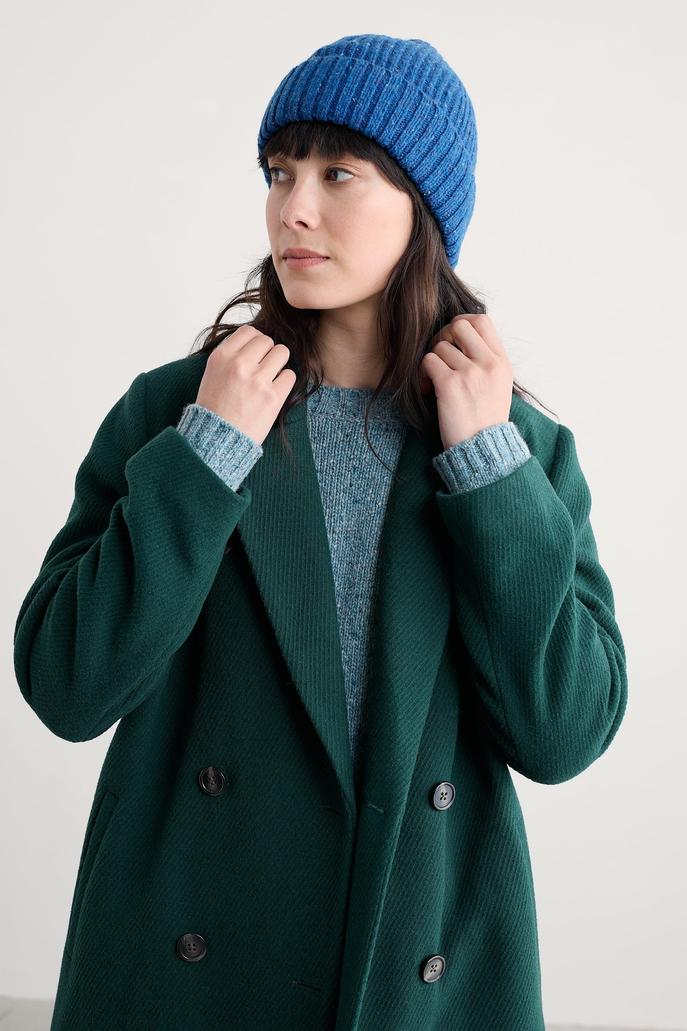 Person wearing a green coat and blue knit hat against a white background