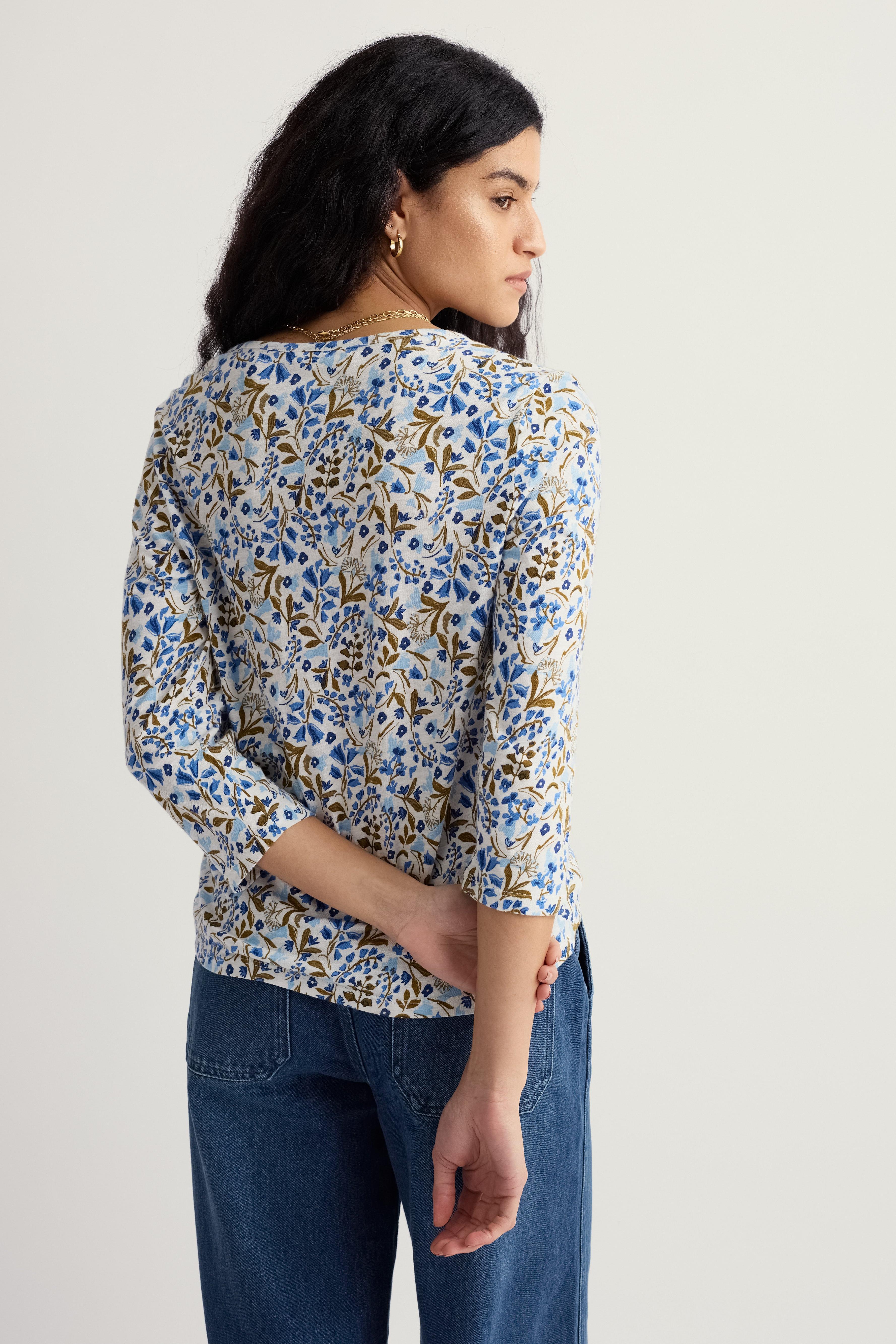 Woman wearing a floral organic cotton blouse and blue jeans against a plain background