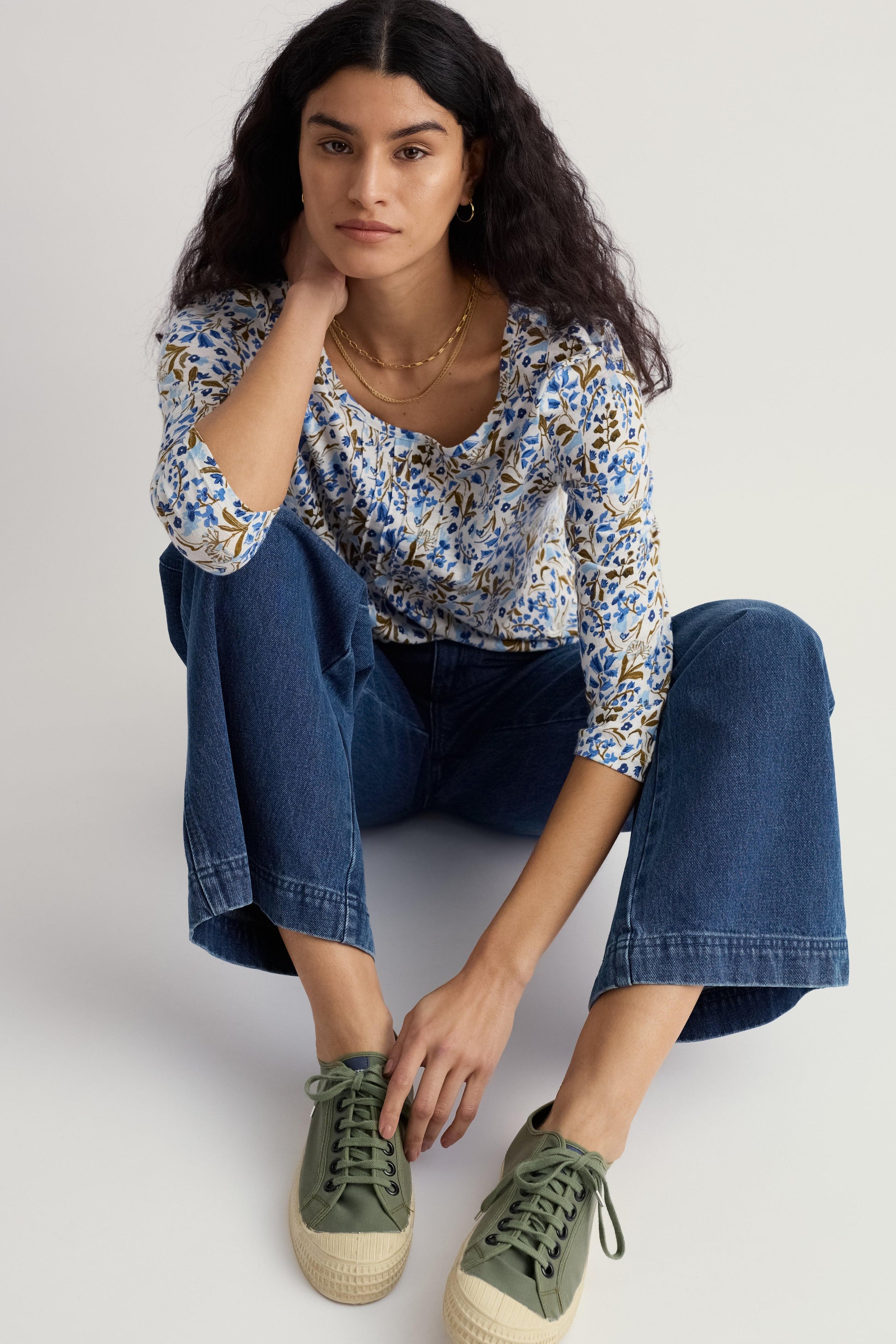 Woman wearing a floral blouse and blue jeans, sitting on a white background