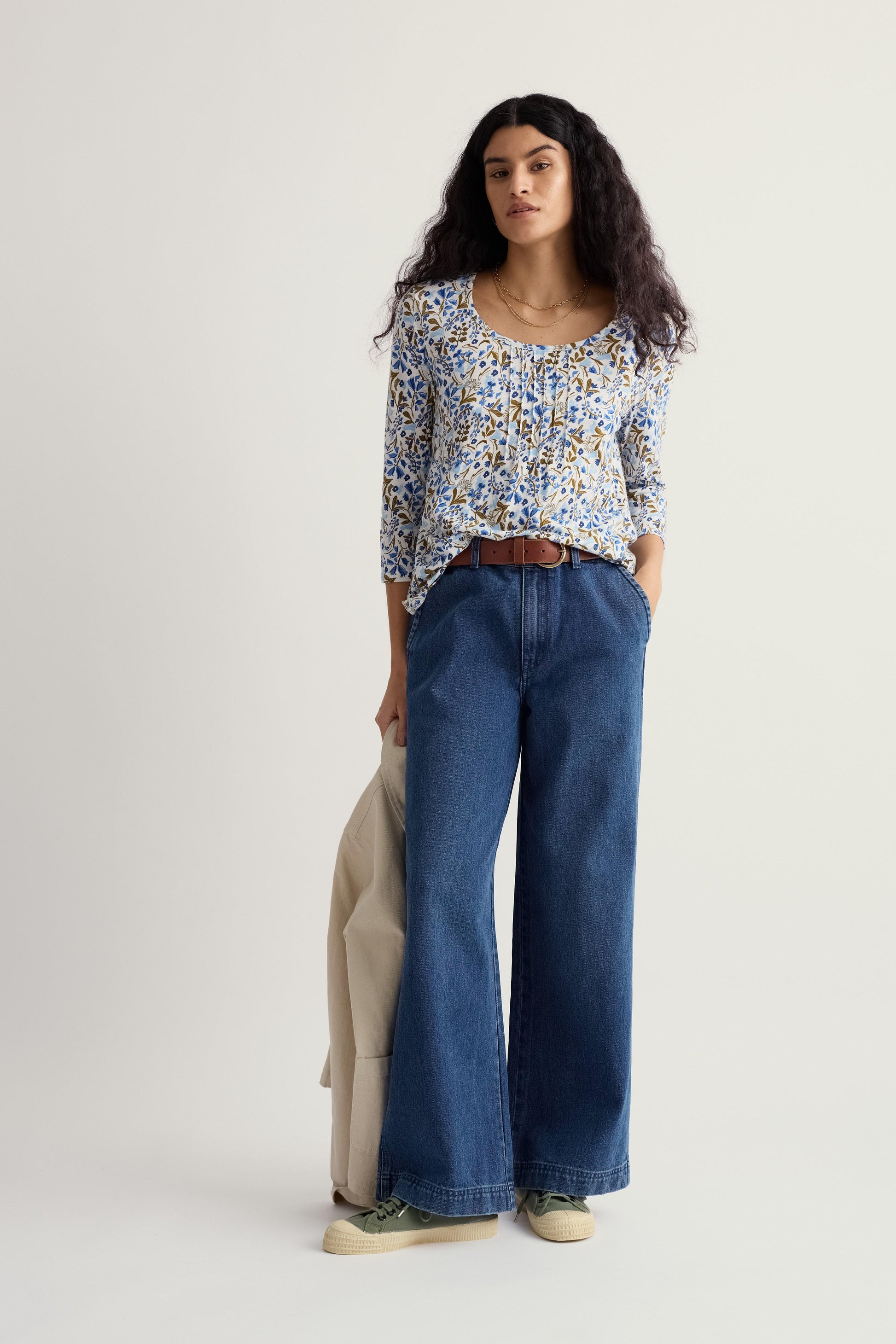 Woman wearing a floral top and blue jeans on a plain background