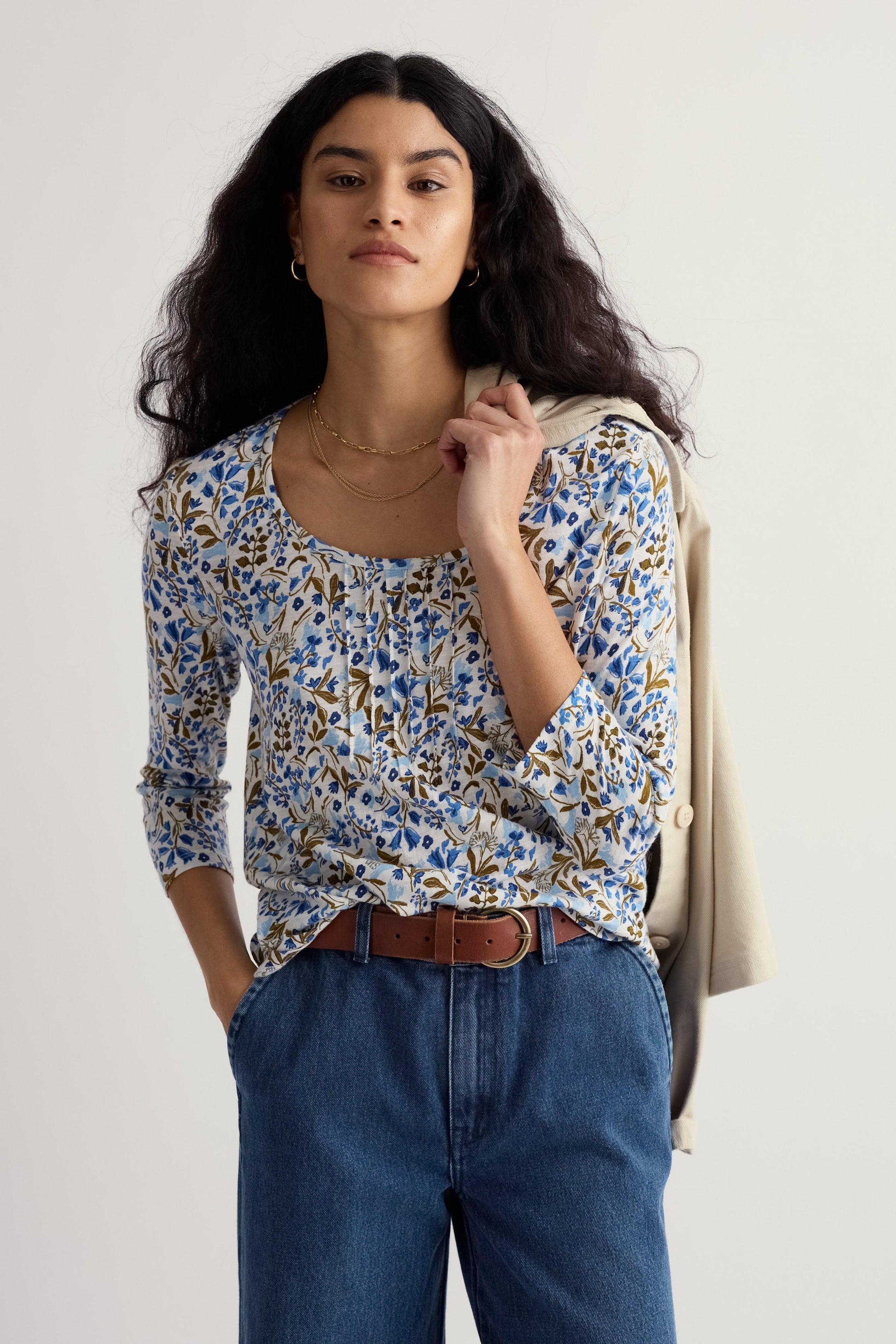 Woman wearing a floral organic cotton blouse and blue jeans against a white background