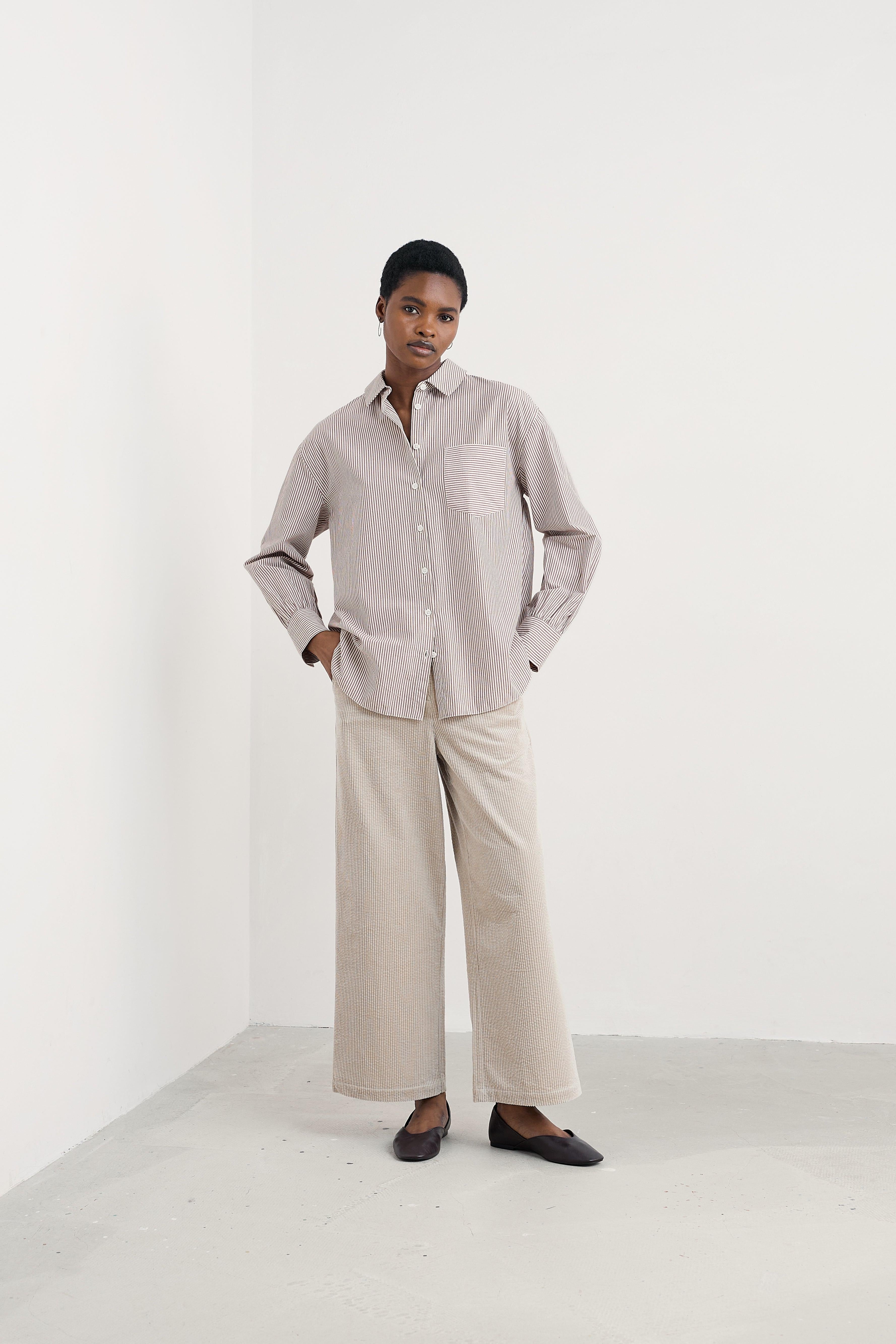 Person wearing a striped shirt and beige pants against a white background