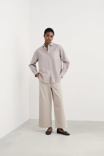 Person wearing a striped shirt and beige pants against a white background