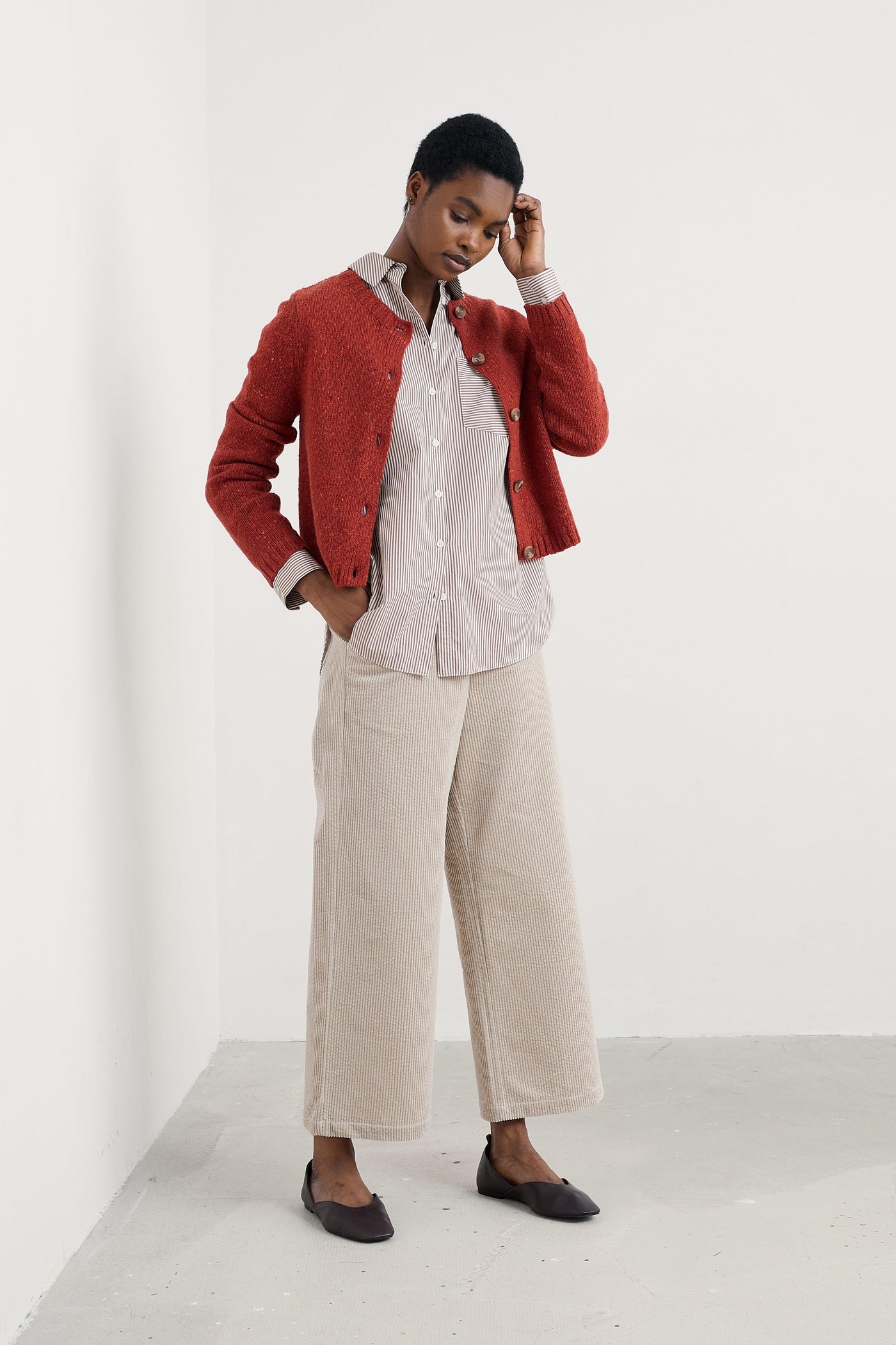 Person wearing a red cardigan, striped organic cotton shirt, beige pants, and black shoes on a white background