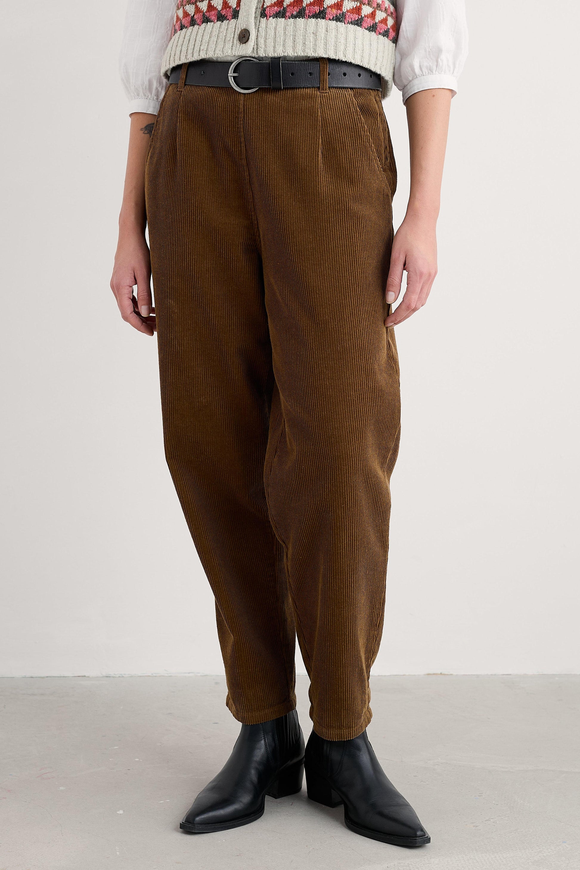 Person wearing brown organic cotton pants and black boots on a white background