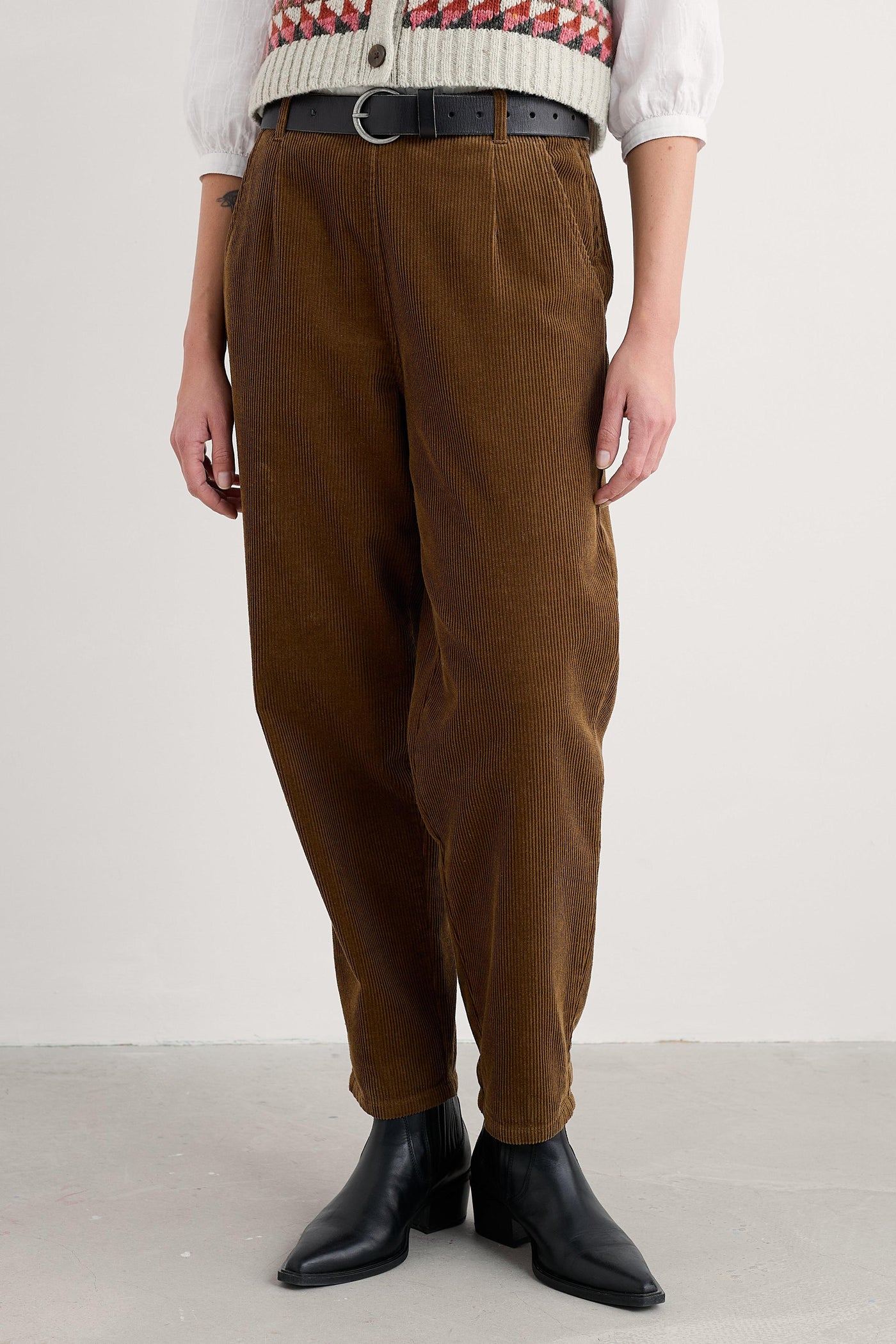 Person wearing brown organic cotton pants and black boots on a white background