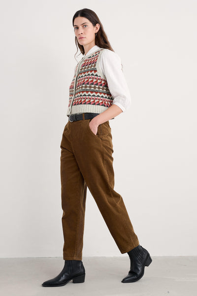Woman wearing a patterned vest, white shirt, brown pants, and black shoes on a white background