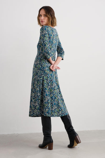 Woman wearing a long, organic cotton patterned dress with black boots on a plain background
