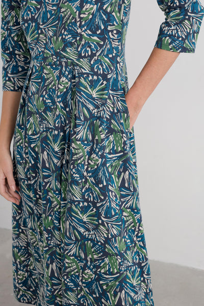 Person wearing a blue and green leaf-patterned dress on a white background